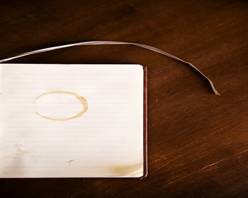 A hot porcelain cup of traditional black coffee sitting on a wooden work desk next to a tiny tray with water