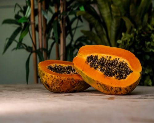 A whole fresh papaya sliced in half displaying its black shiny seeds on a bright stone market countertop