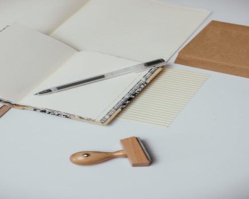 A clean workspace table with an opened leather notepad, a wooden pen, and small organic elements