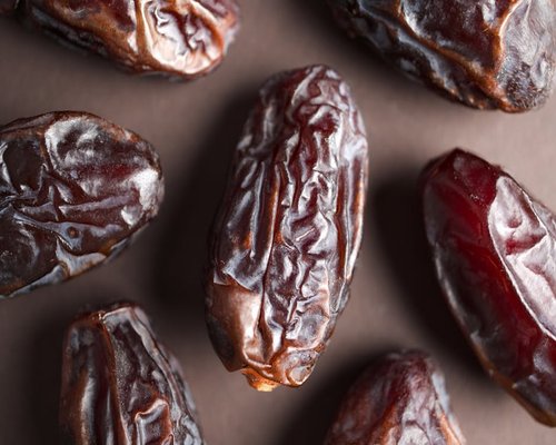 Plump brown Medjool dates grouped together tightly on a rustic dark slate display surface