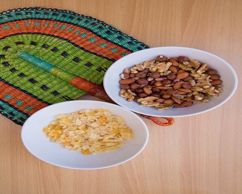 A vibrant mix of dried mango slices, almonds, and walnuts tossed inside a modern light ceramic bowl